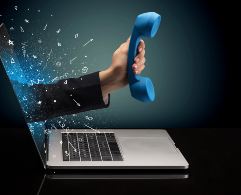 Hand holding a telephone receiver emerging from a laptop screen